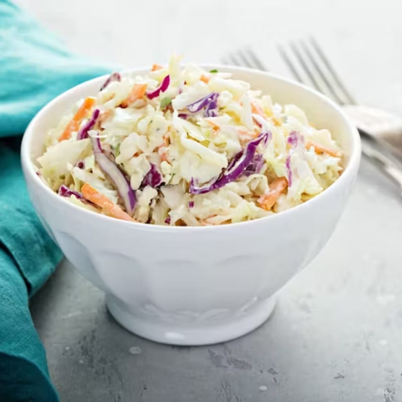 A white bowl filled with creamy coleslaw, featuring shredded cabbage, carrots, and red cabbage.