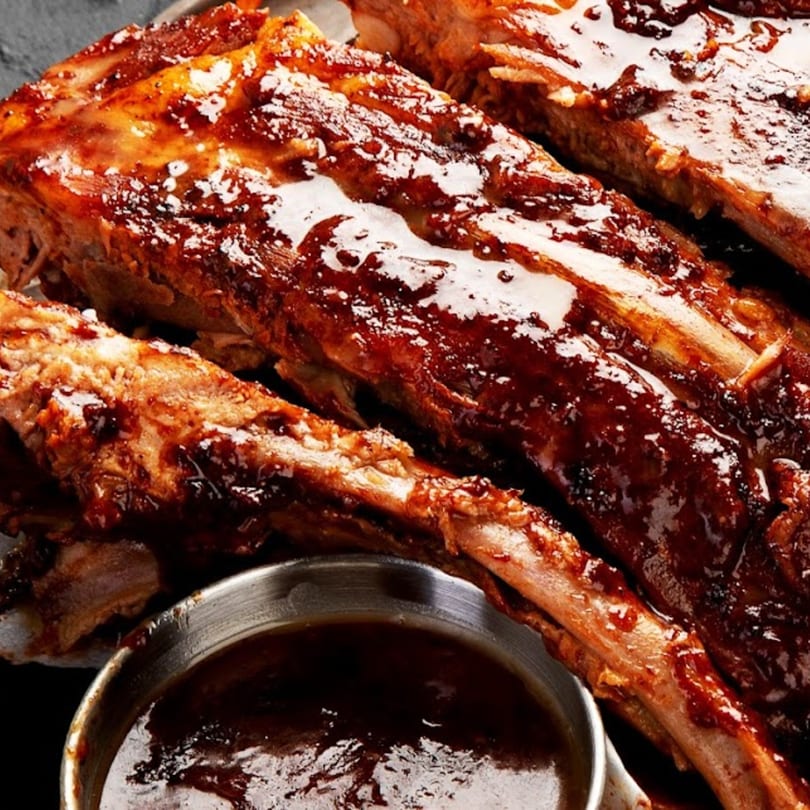 Close-up of Big Orange BBQ's glistening, saucy ribs with a side of barbecue sauce.
