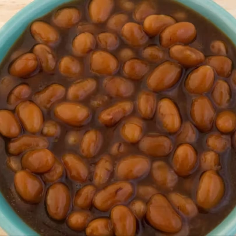Close-up of Big Orange BBQ's baked beans in a light blue bowl, glistening in a rich brown sauce.
